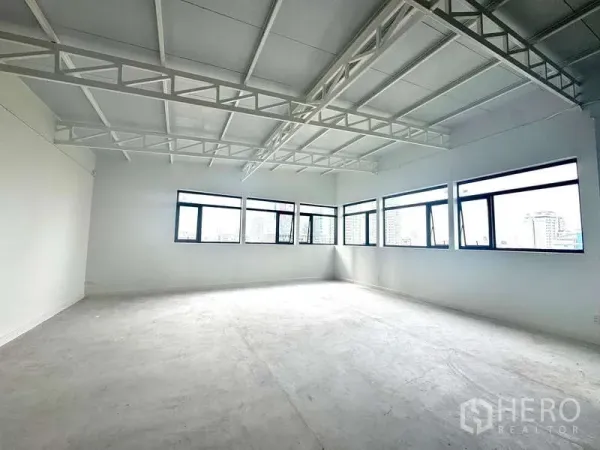 Office Space for rent in Bang Rak, Bangkok - Bright open-plan 100 sqm office with exposed truss ceiling and multiple corner windows overlooking the Bang Rak skyline.