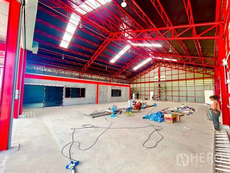 货栈 出租在Lam Luk Ka, Pathum Thani - 无柱大空间仓库内景，红色结构，地面摆放施工材料。