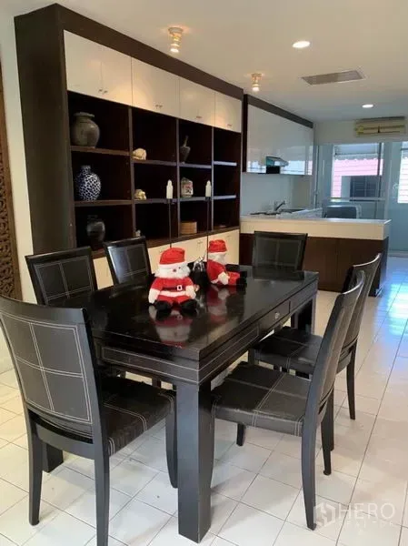 Townhouse for rent in Khlong Toei, Bangkok - Dining area with dark wood table and six chairs beside built‑in shelving and an open kitchen.