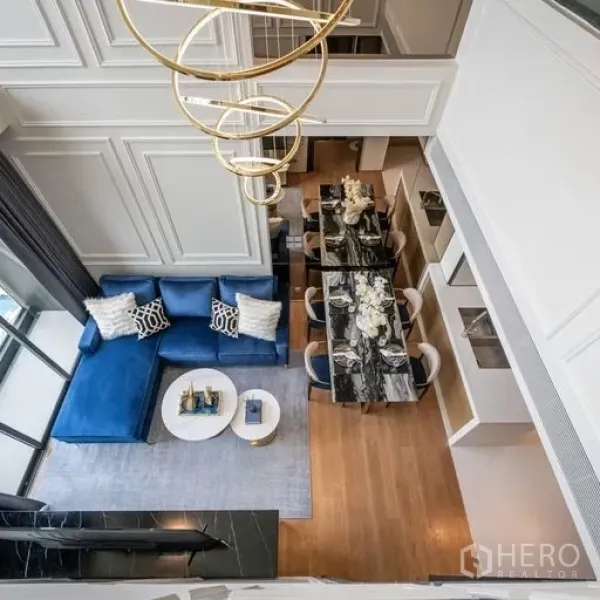 คอนโด ให้เช่าในKhlong Toei, Bangkok - มุมมองจากด้านบนของโถงนั่งเล่นเพดานสูงพร้อมโซฟาสีน้ำเงิน โต๊ะทานหินอ่อน พื้นไม้ และโคมไฟทรงวงกลมสีทอง