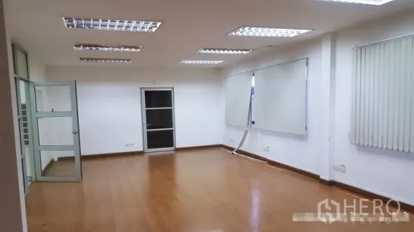 Warehouse for rent in Suan Luang, Bangkok - Empty office room with wood flooring, blinds, and recessed fluorescent lights.