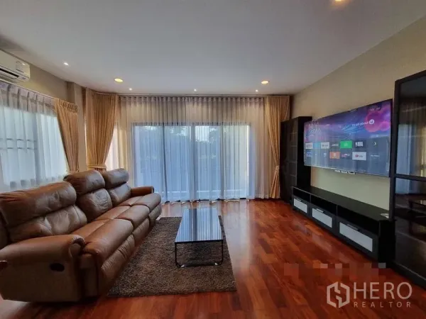 Detached House for rent in Bang Khae, Bangkok - Bright living room with leather sofa, wood flooring, large TV and sliding glass doors.