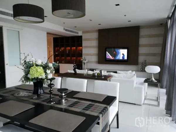 Condominium for rent in Pathum Wan, Bangkok - Dining table facing lounge with TV feature wall and illuminated built-in shelving.