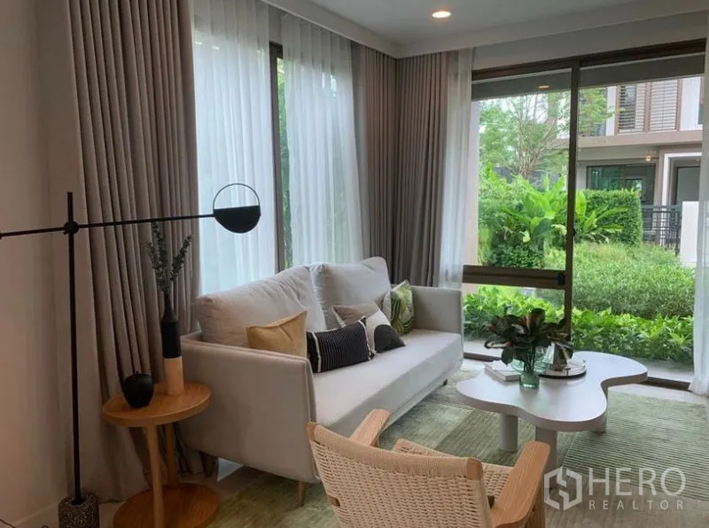 独立式住宅 出售在Bang Kapi, Bangkok - 采光充足的客厅，沙发与落地窗，面向绿意花园的现代空间。