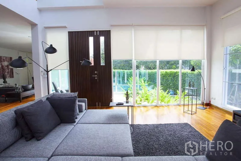 独立式住宅 出租在Lat Phrao, Bangkok - 客厅面向入户门与整面玻璃墙，眺望泳池与花园。