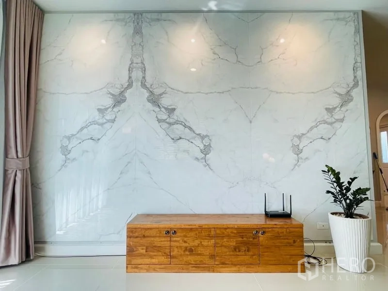 บ้าน ขายในLam Luk Ka, Pathum Thani - ผนังห้องนั่งเล่นลายหินอ่อนพร้อมตู้วางทีวีไม้และกระถางต้นไม้