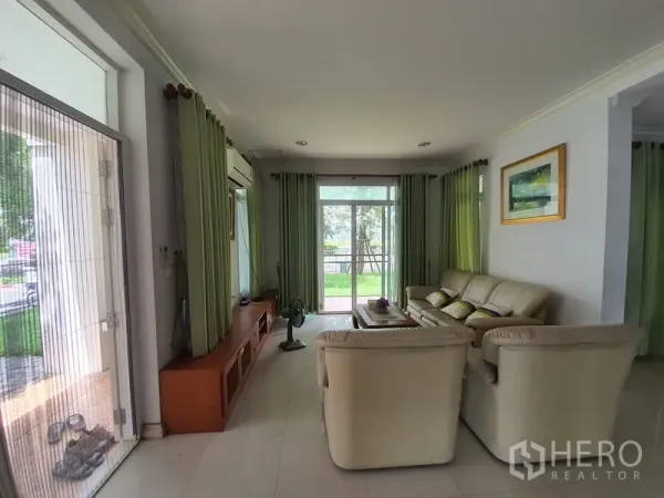 บ้าน ให้เช่าในLat Krabang, Bangkok - ห้องนั่งเล่นสว่าง ชุดโซฟาสีครีม ตู้ทีวีบิวต์อิน และประตูกระจกเปิดสู่สวน.