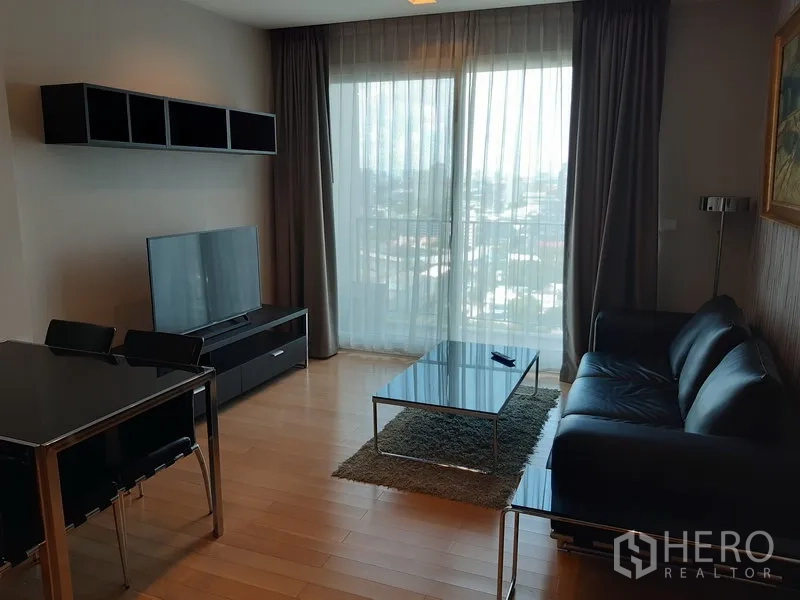 公寓 出租在Khlong Toei, Bangkok - 明亮客厅，落地窗与城市景观阳台，沙发、电视柜和餐桌。