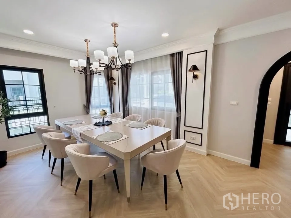 Detached House for rent in Bang Phli, Samut Prakan - Dining room with chandelier lighting and an eight-seat table by wide windows and curtains.