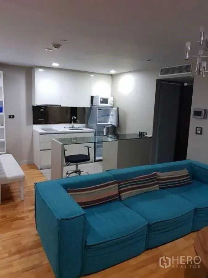 Condominium for sale in Bang Rak, Bangkok - Open living and kitchen space with teal sofa and white cabinetry.