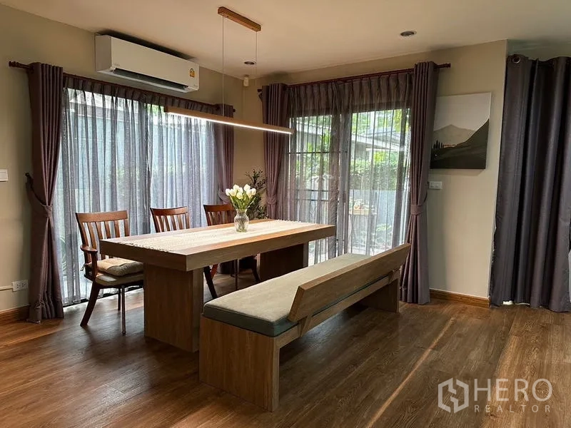 独立式住宅 出租在Prawet, Bangkok - 餐厅，长吊灯、长凳座与透光窗帘面向花园。