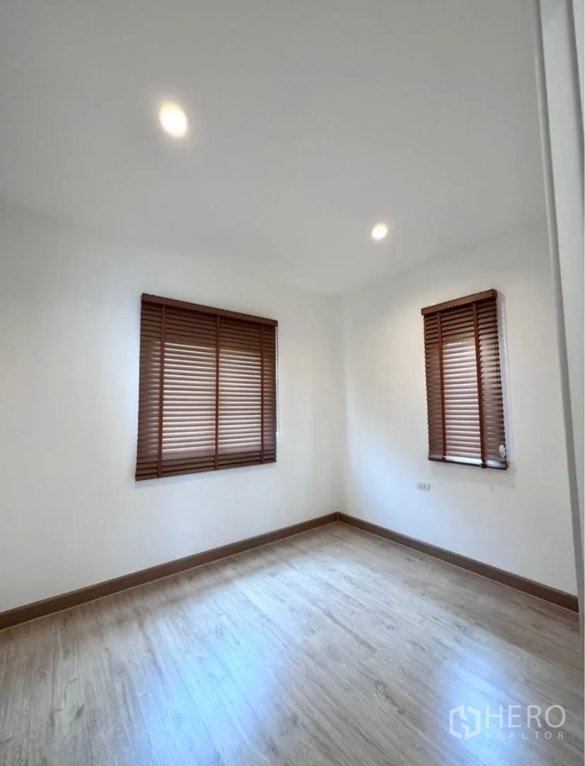 Detached House for rent in Samut Prakan - Empty bedroom with wood flooring and two windows with blinds.