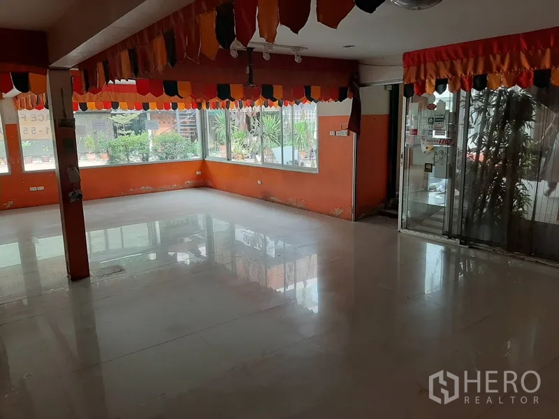 零售空间 出租在Watthana, Bangkok - 转角展厅，大幅落地窗，橙色点缀墙面与亮面地砖。