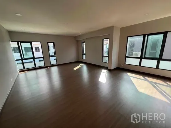 Detached House for rent in Khlong Sam Wa, Bangkok - Spacious empty living room with wood flooring and multiple black-framed windows bringing in natural light.