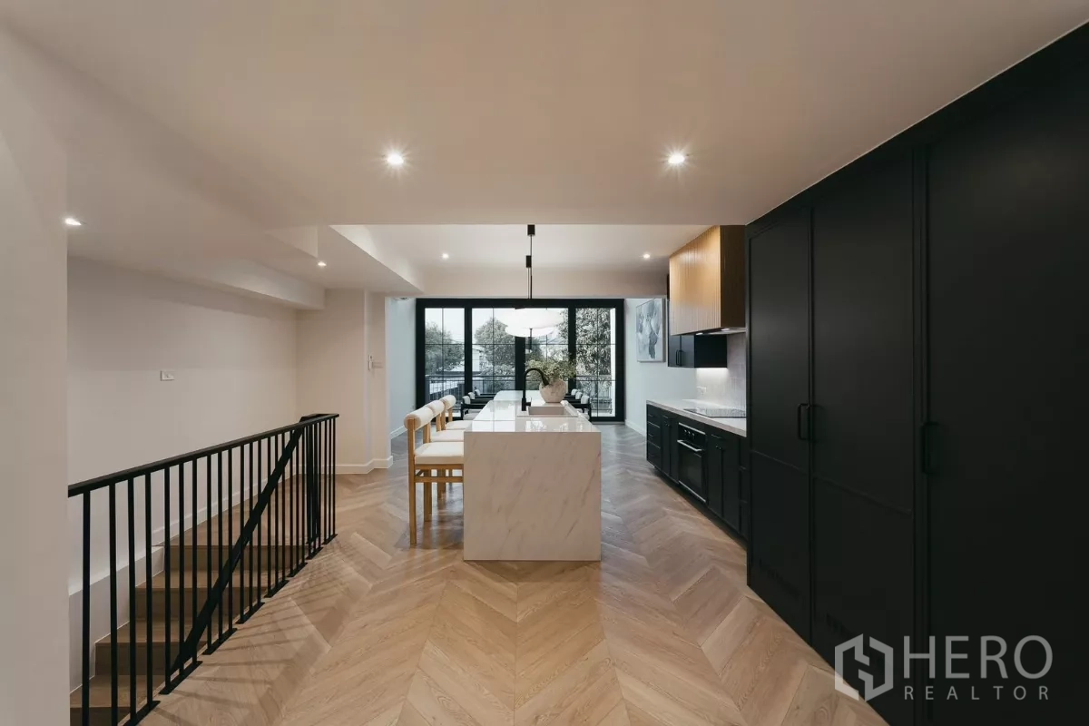 联排别墅 出租在Watthana, Bangkok - 纵深厨房，中岛、鱼骨拼木地板与通向阳台的玻璃门。