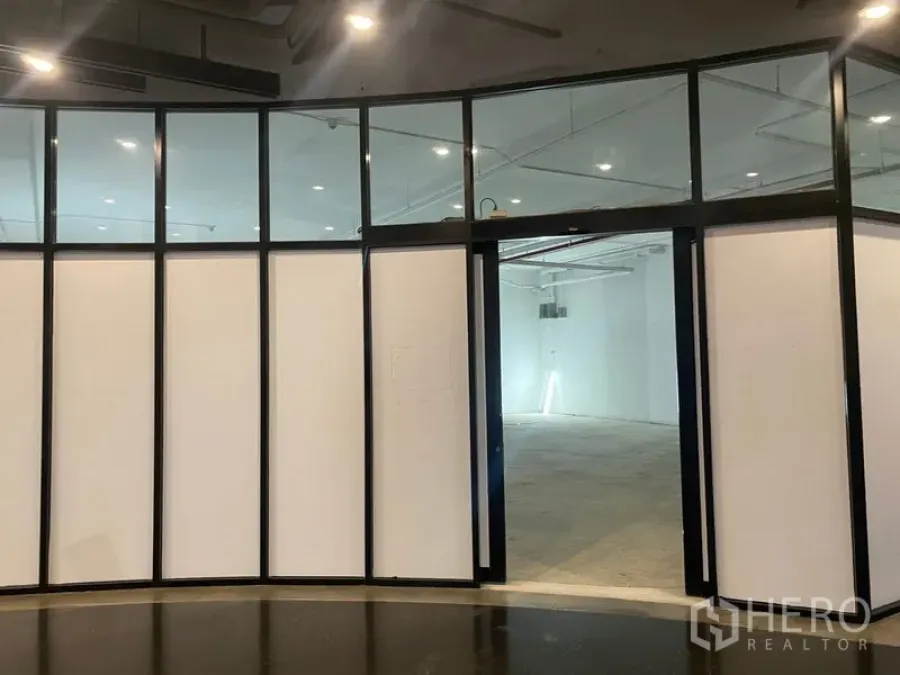 พื้นที่ขายปลีก ให้เช่า - หน้าร้านกระจกโค้งกรอบสีดำ เปิดสู่พื้นที่เปล่าโทนขาวพร้อมไฟดาวน์ไลท์