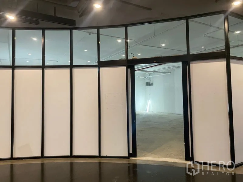 พื้นที่ขายปลีก ให้เช่า - หน้าร้านกระจกโค้งกรอบสีดำ เปิดสู่พื้นที่เปล่าโทนขาวพร้อมไฟดาวน์ไลท์