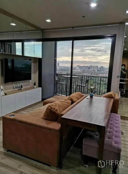 Condominium for rent - Living area with dining table behind the sofa and large balcony doors framing Chatuchak park and skyline views at dusk.
