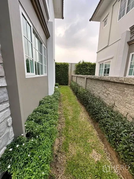 Detached House for rent - Side garden with flower beds, stone boundary wall, and neighboring homes.
