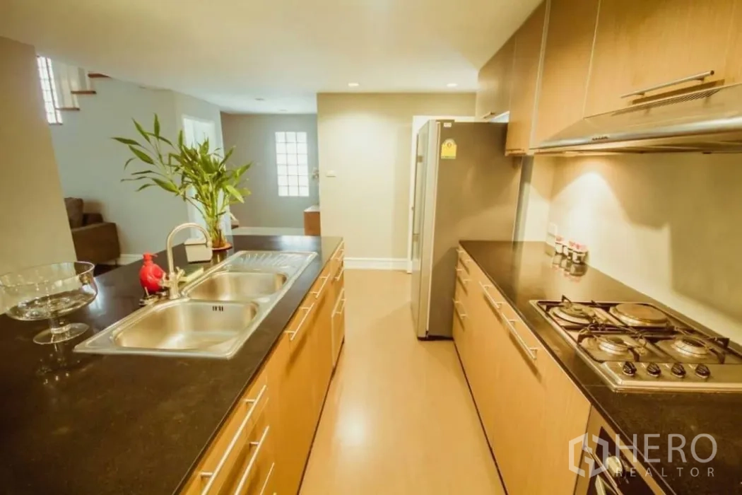 บ้าน ให้เช่าในKhlong Toei, Bangkok - ภาพระยะใกล้ของไอแลนด์ครัวพร้อมอ่างล้างจานคู่ เคาน์เตอร์หิน และตู้ไม้บิวท์อินกับเตา.