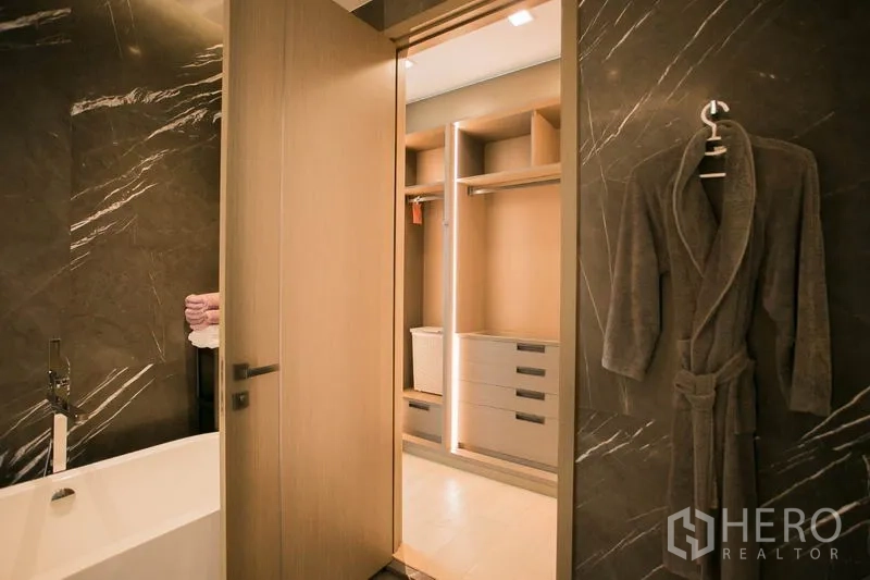 Condominium for rent or sale in Watthana, Bangkok - Ensuite with dark marble walls and soaking tub opening to illuminated walk-in wardrobe.