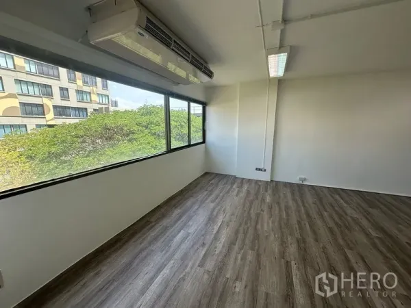 办公空间 出租在Bangkok - 角落办公区，整排宽窗可见绿树景观，窗边挂壁式空调。