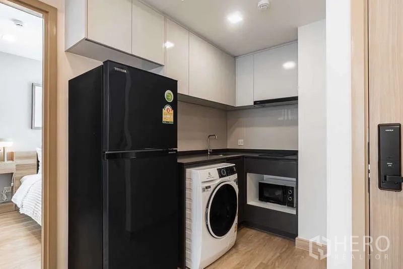 คอนโด ให้เช่า - ครัวรูปตัวแอลสมัยใหม่พร้อมตู้เย็นสีดำ เครื่องซักผ้า และไมโครเวฟบิวต์อิน