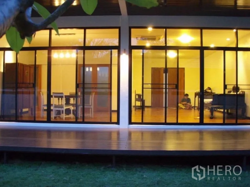 บ้าน ให้เช่าในHuai Khwang, Bangkok - ภาพมุมค่ำของบ้านชั้นเดียวสมัยใหม่ ผนังกระจกเต็มบาน ระเบียงไม้และสนามหญ้า