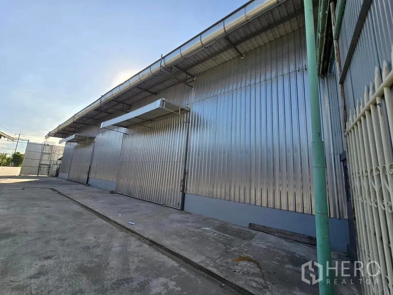 货栈 出租在Sai Noi, Nonthaburi - 波纹金属墙体侧立面，可见多处服务门、排水天沟与硬化院坪。