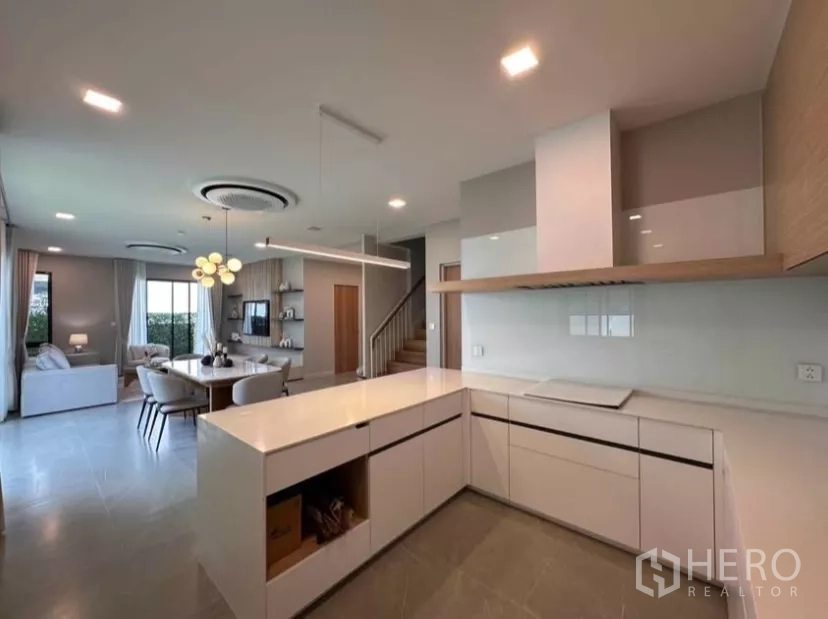 Detached House for rent in Samut Prakan - Sleek white L-shaped kitchen and dining space in a modern open layout.