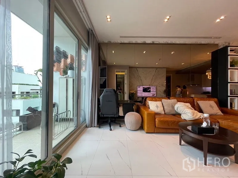 Condominium for rent in Pathum Wan, Bangkok - Sliding glass doors open to terrace beside study nook and tan sofa in open-plan lounge.