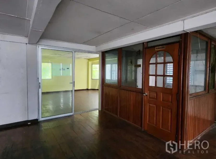 零售空间 出租在Bang Rak, Bangkok - 室内走廊配深色木地板，玻璃隔断办公室与拱形木门，旁边为通往明亮房间的推拉玻璃门。