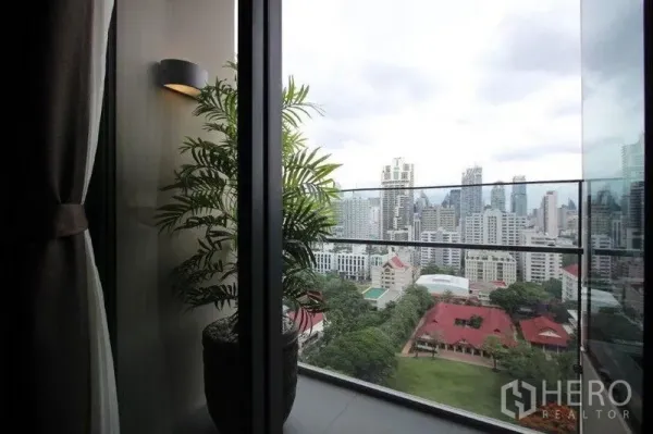 Condominium for rent in Watthana, Bangkok - Glass balcony with potted plant overlooking the Asok skyline and green park views.