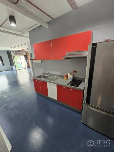Office Space for rent in Watthana, Bangkok - Compact kitchenette with red cabinets, cooktop, range hood, sink, and fridge opening to the office space.