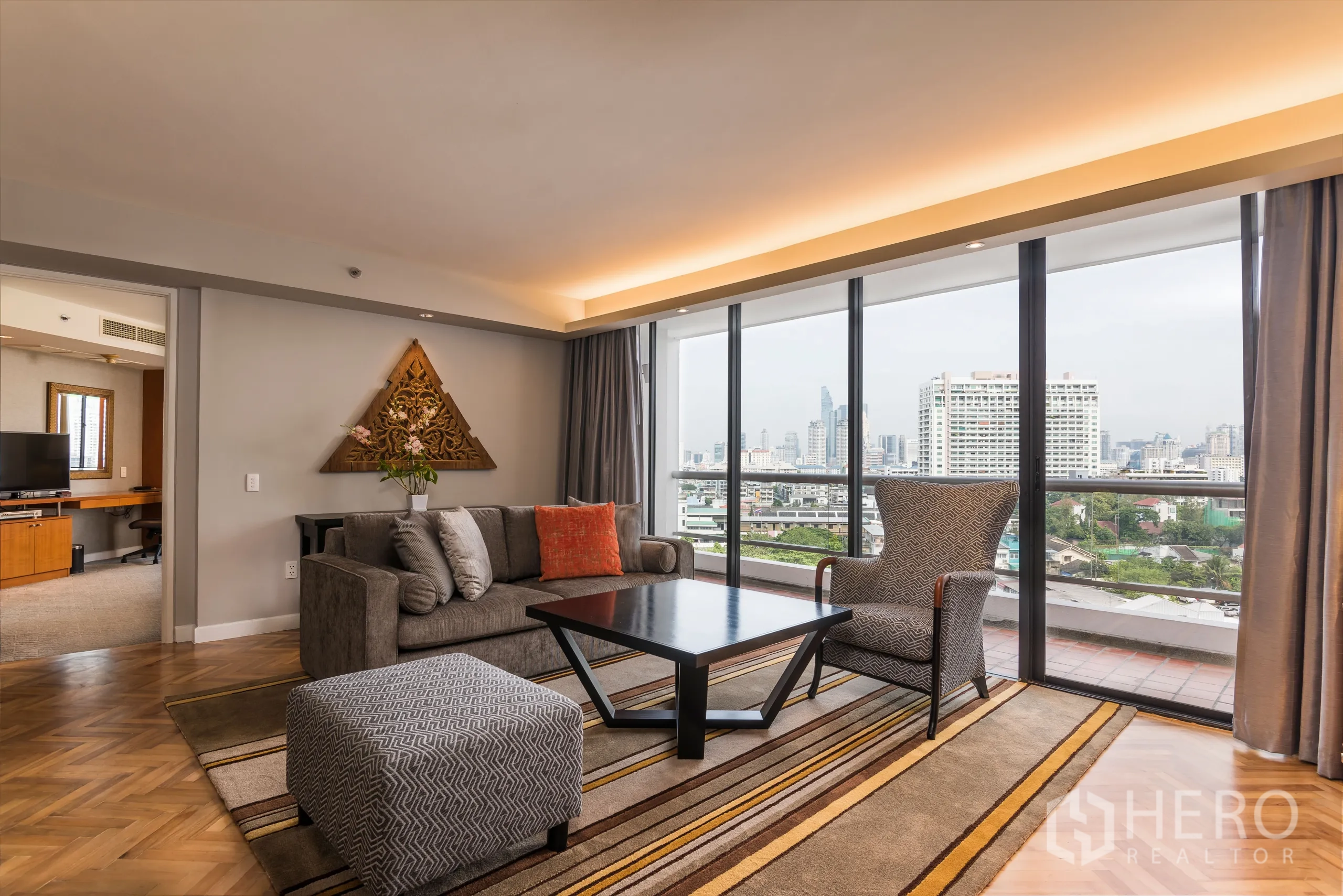 Condominium for rent in Yan Nawa, Bangkok - Comfortable living area with sofa set and patterned rug facing floor-to-ceiling glass doors to a balcony overlooking the city.