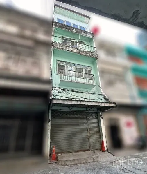 Shophouse for rent in Khlong Toei, Bangkok - Four-storey mint-green shophouse facade with balconies and a roller shutter storefront on a side street.