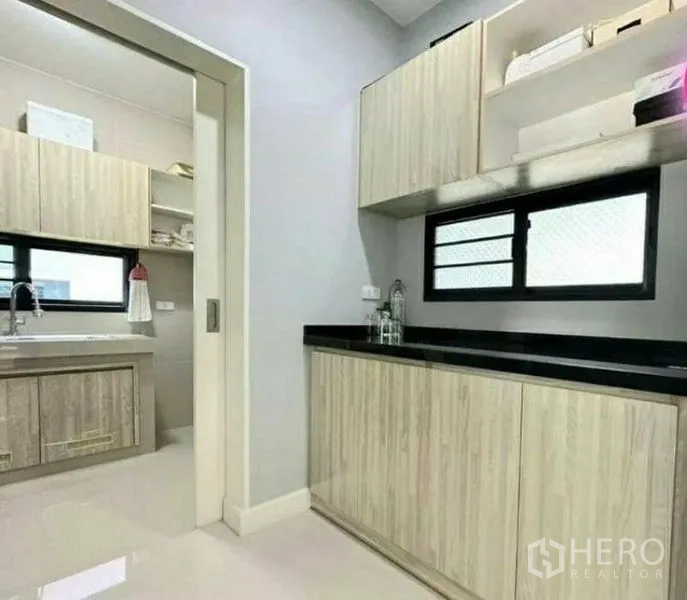 Detached House for sale in Pathum Thani - Modern kitchen with light wood cabinetry, black countertops and a separate wet kitchen.