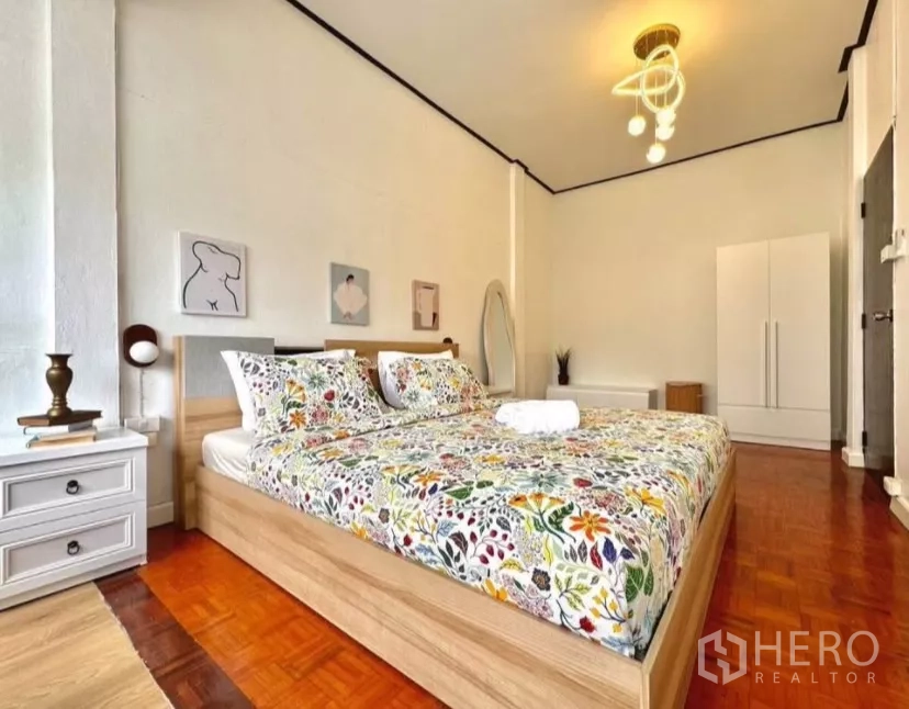 Townhouse for rent in Watthana, Bangkok - Spacious bedroom with floral bedding, pendant light, wardrobe and parquet floors.