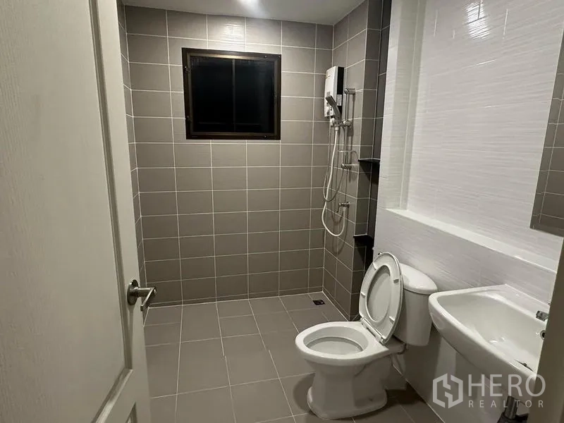 Detached House for rent in Bang Phli, Samut Prakan - Second bathroom with gray tiles, toilet, sink and shower area.