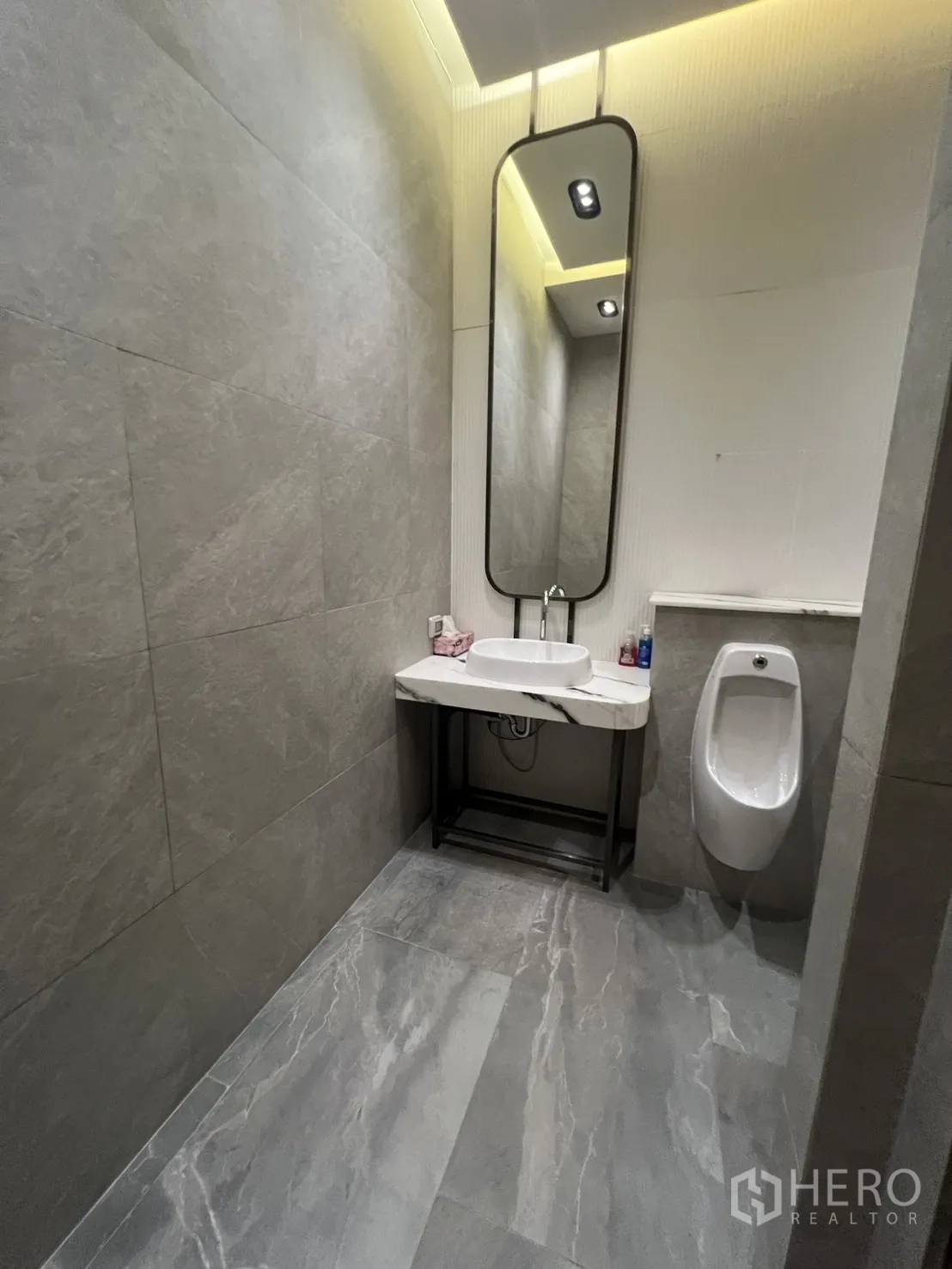 零售空间 出租 - 现代卫生间，长镜、台盆、小便斗与灰色石材瓷砖。