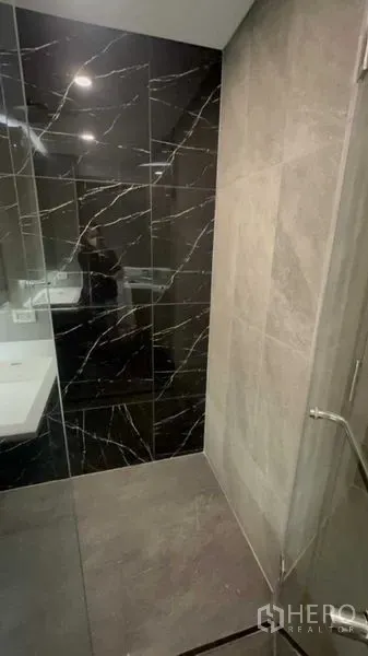 Condominium for sale in Huai Khwang, Bangkok - Walk-in shower with glass door and black marble feature wall.