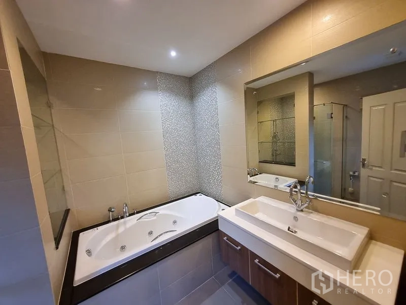 Detached House for rent in Bang Khae, Bangkok - Bathroom angle showing the bathtub, large mirror, and countertop sink.