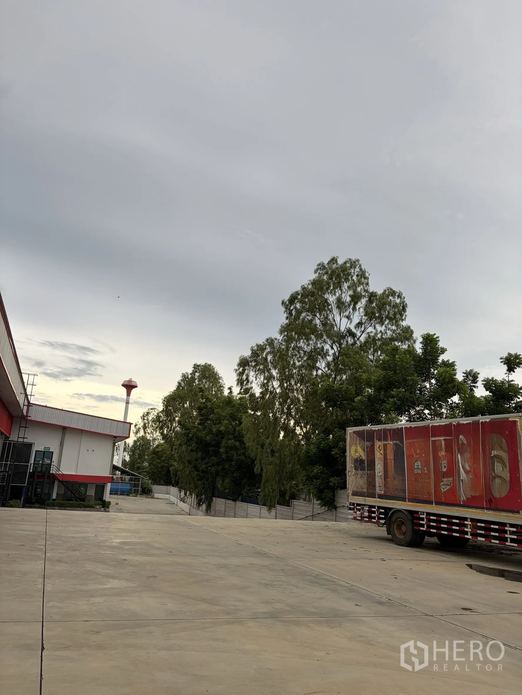Factory for sale in Mueang Nakhon Pathom, Nakhon Pathom - Open yard with mature trees and parked trailer beside factory.