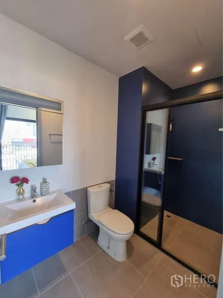 公寓 出租在Watthana, Bangkok - 宽敞浴室，蓝色特色墙，玻璃淋浴间、洗手台与马桶。