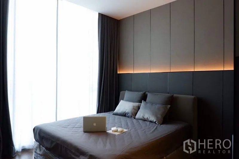 Condominium for sale in Khlong Toei, Bangkok - Cozy bedroom with upholstered headboard, warm ambient lighting, and full-height drapes.
