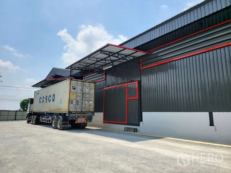Warehouse for rent in Sam Phran, Nakhon Pathom - Modern warehouse exterior in Sam Phran with a covered loading bay and a container truck at the dock.