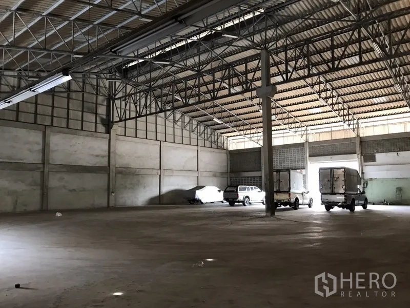 Warehouse for rent in Mueang Samut Prakan, Samut Prakan - Open storage area showing wide column spacing, ventilated block walls, and trucks under a high gabled roof.