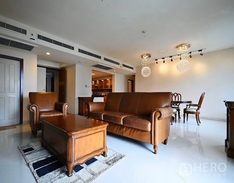 Condominium for rent in Pathum Wan, Bangkok - Bright living room with brown leather sofa set, wooden coffee table, and crystal pendant lights beside the dining area.
