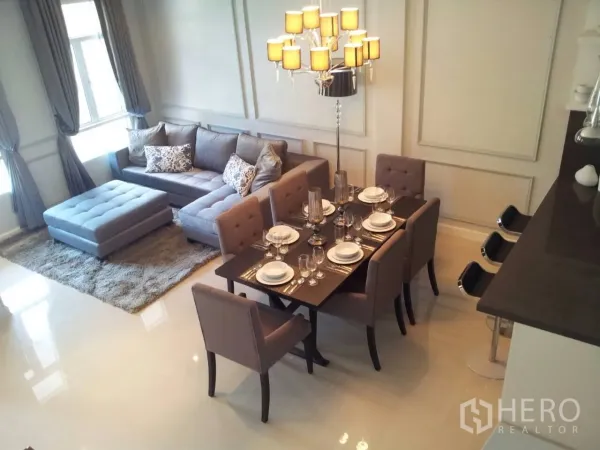 联排别墅 出租在Watthana, Bangkok - 开放式客餐厅，灰色转角沙发、吊灯与六人餐桌。