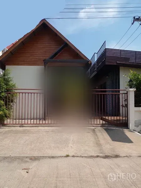 Shophouse for sale in Lam Luk Ka, Pathum Thani - Gated front exterior with driveway and gabled-roof building.